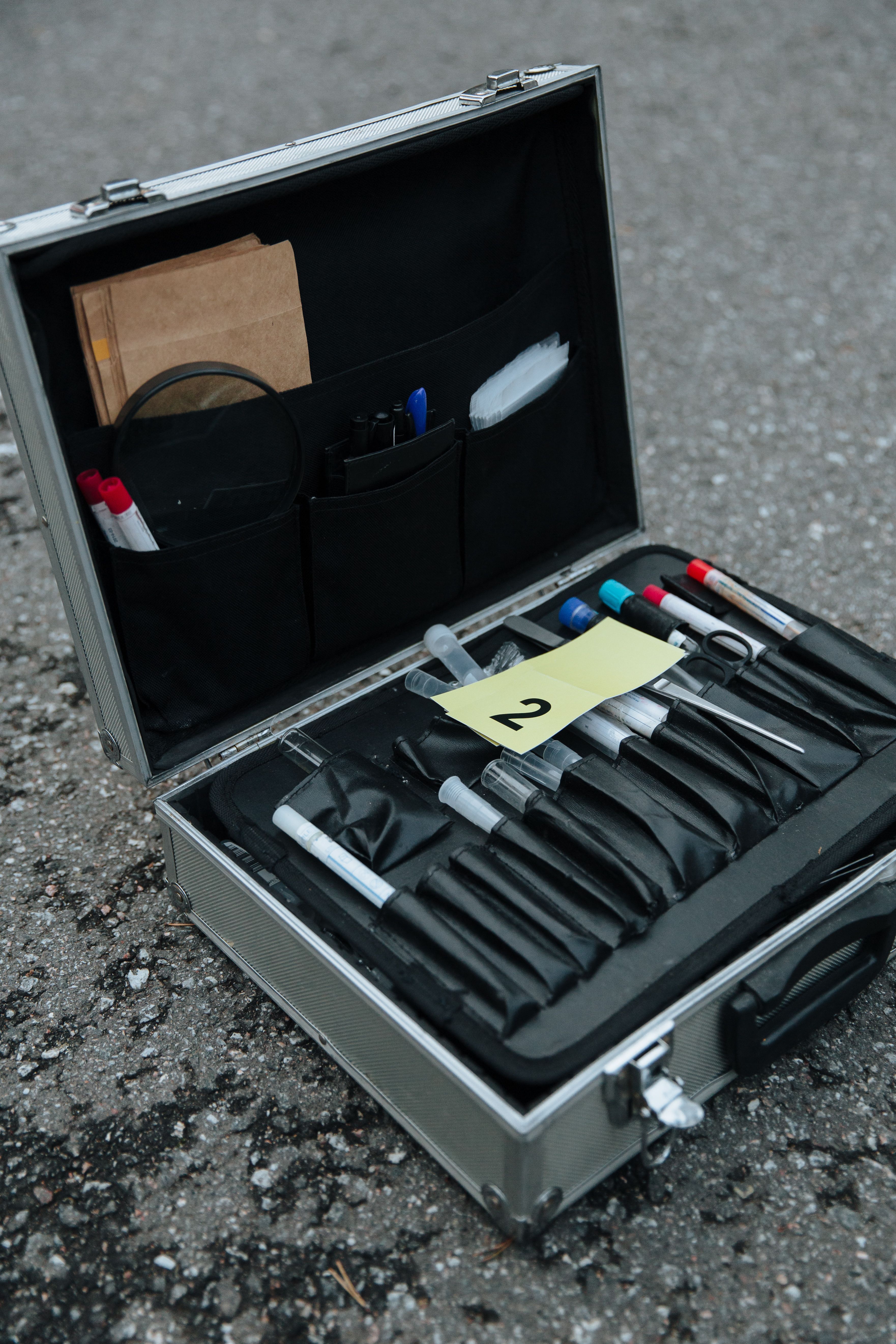 Open forensic evidence case with tools on a city asphalt street, numbered tag visible.