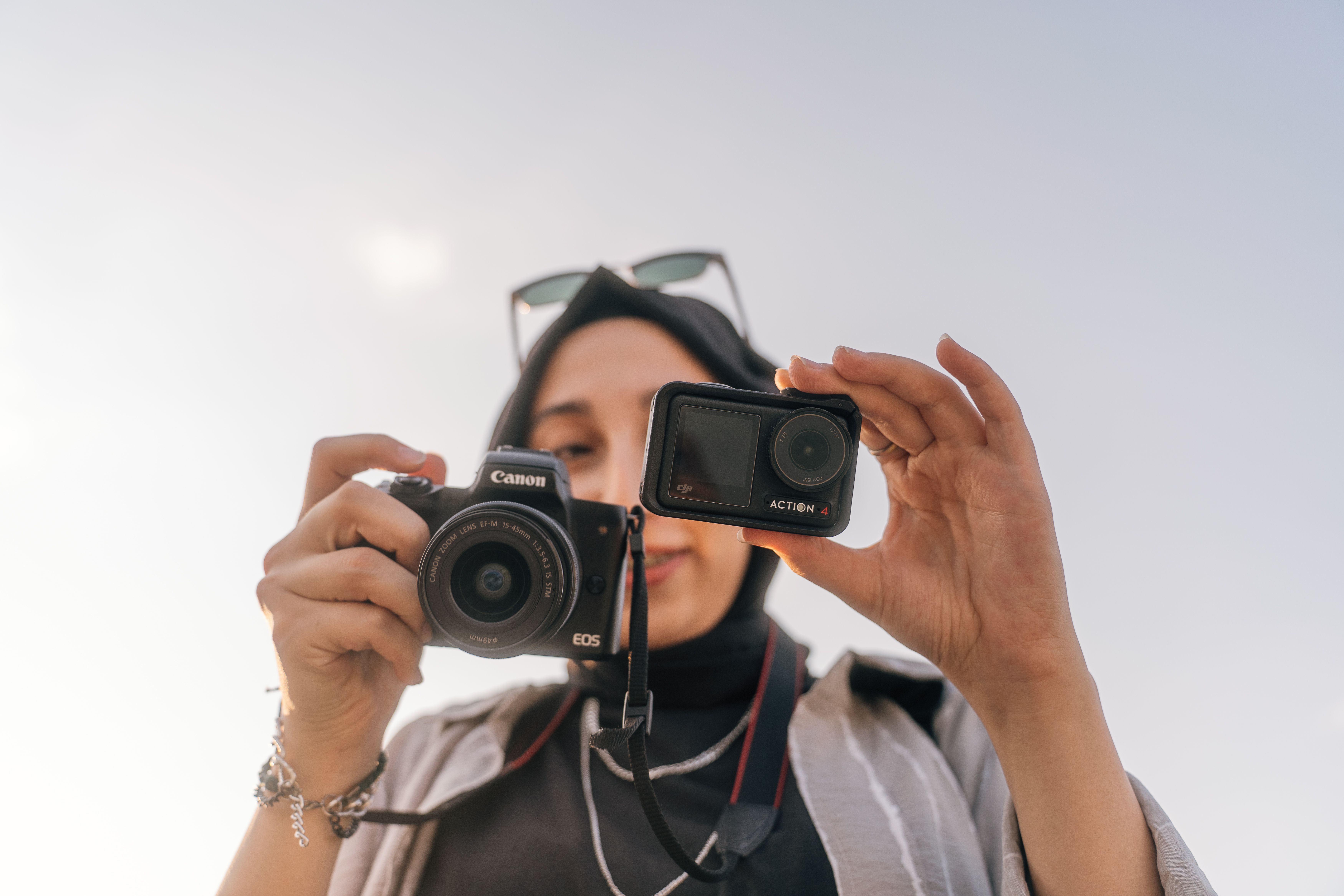 A female photographer showcases two different cameras under a clear sky, depicting modern photography technology.