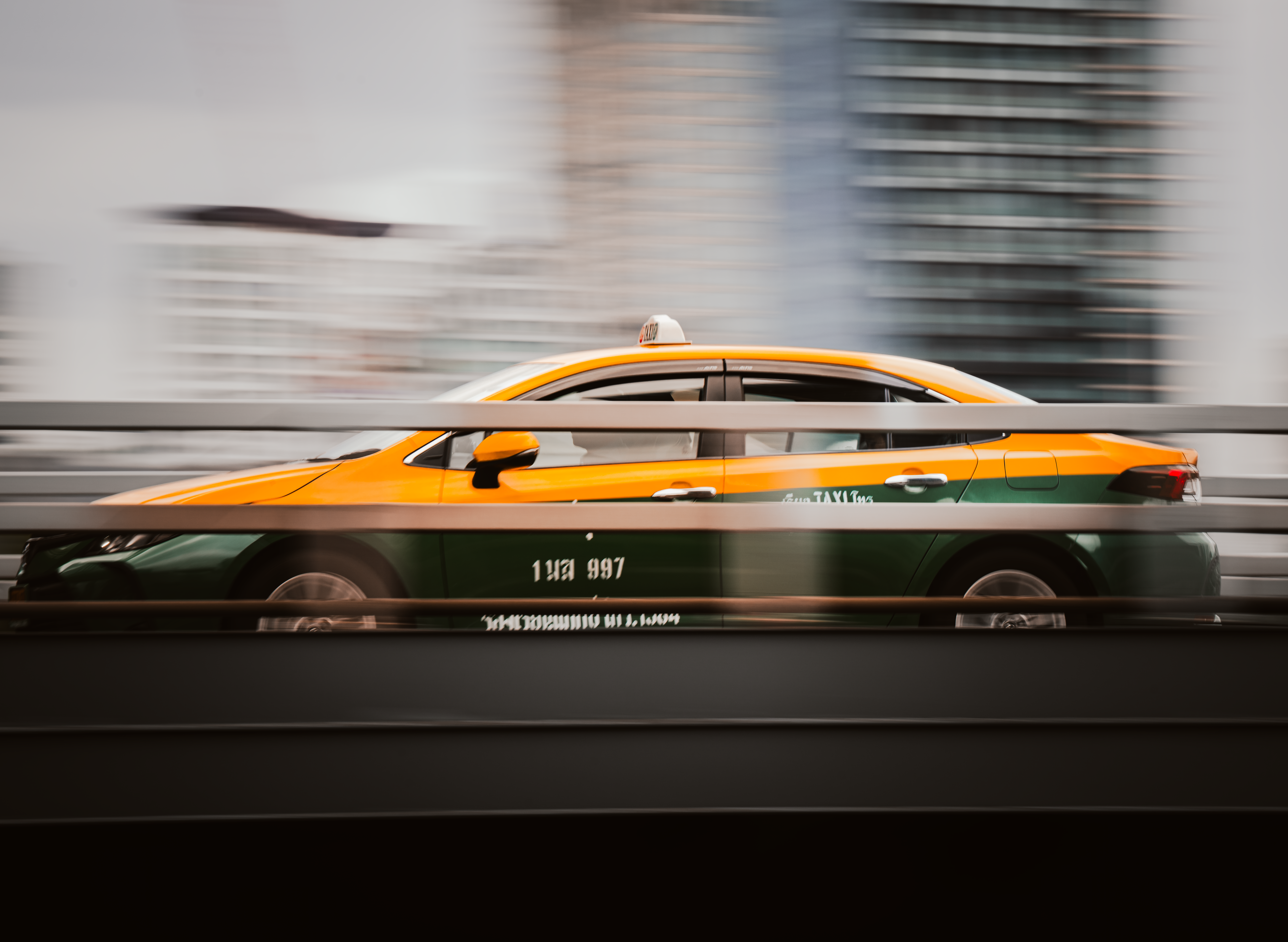 A yellow and green Bangkok taxi speeds through city streets, captured with motion blur.