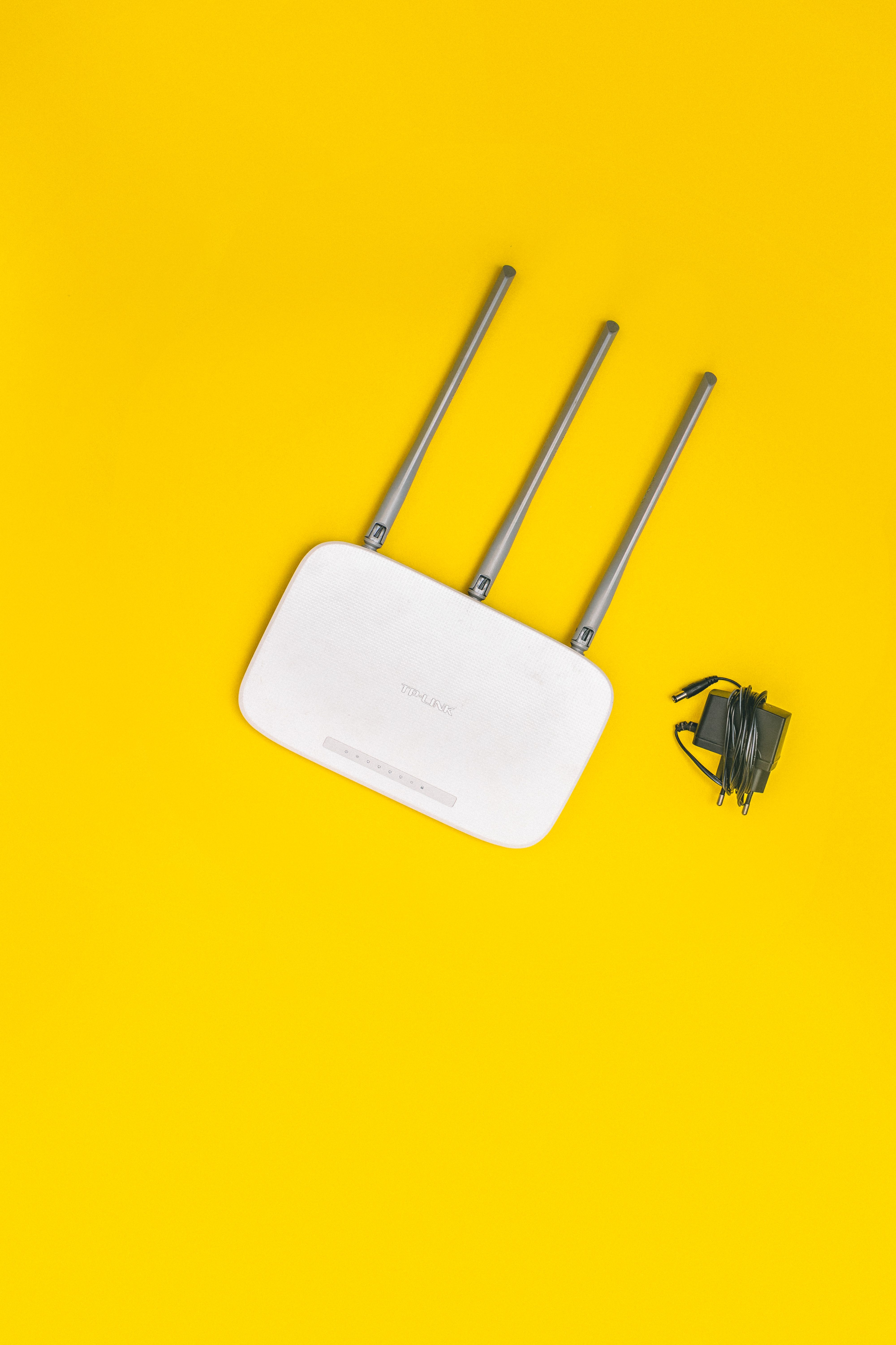 White router with three antennas and cables on bold yellow background, ideal for tech concepts.
