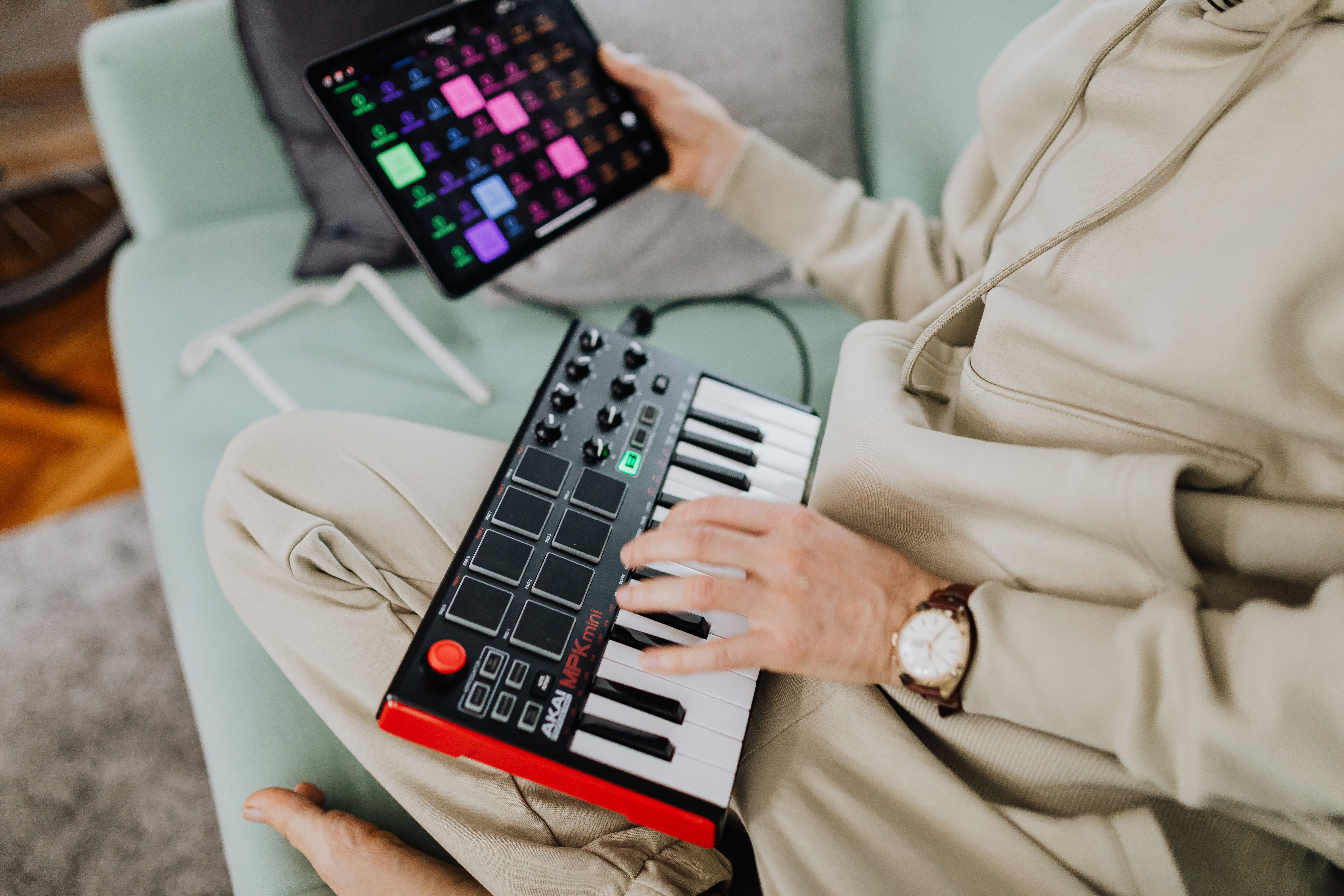 A man sits on a sofa using a MIDI keyboard and tablet for electronic music production. Close-up view.
