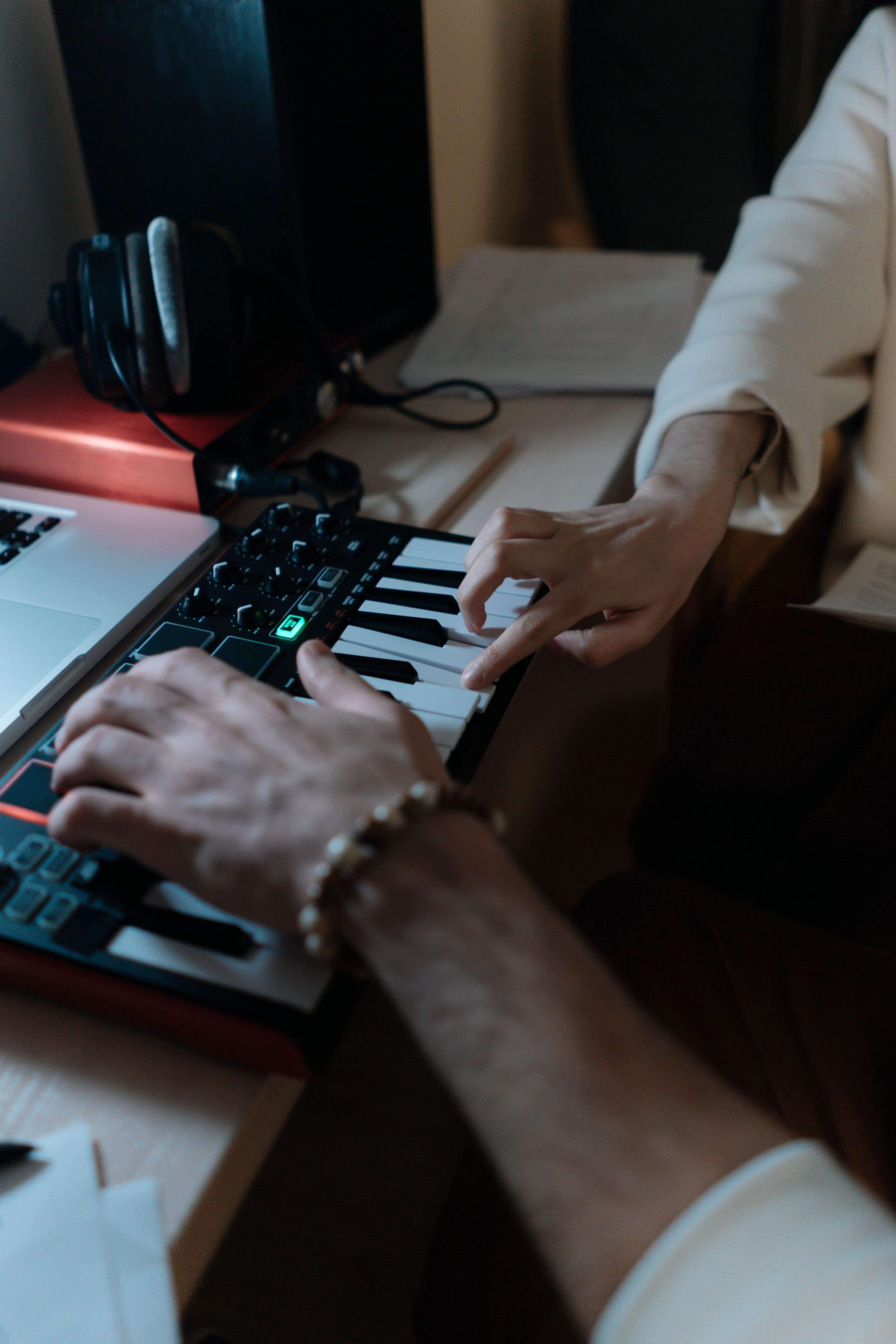 Hands playing a MIDI keyboard connected to a laptop in a music studio.