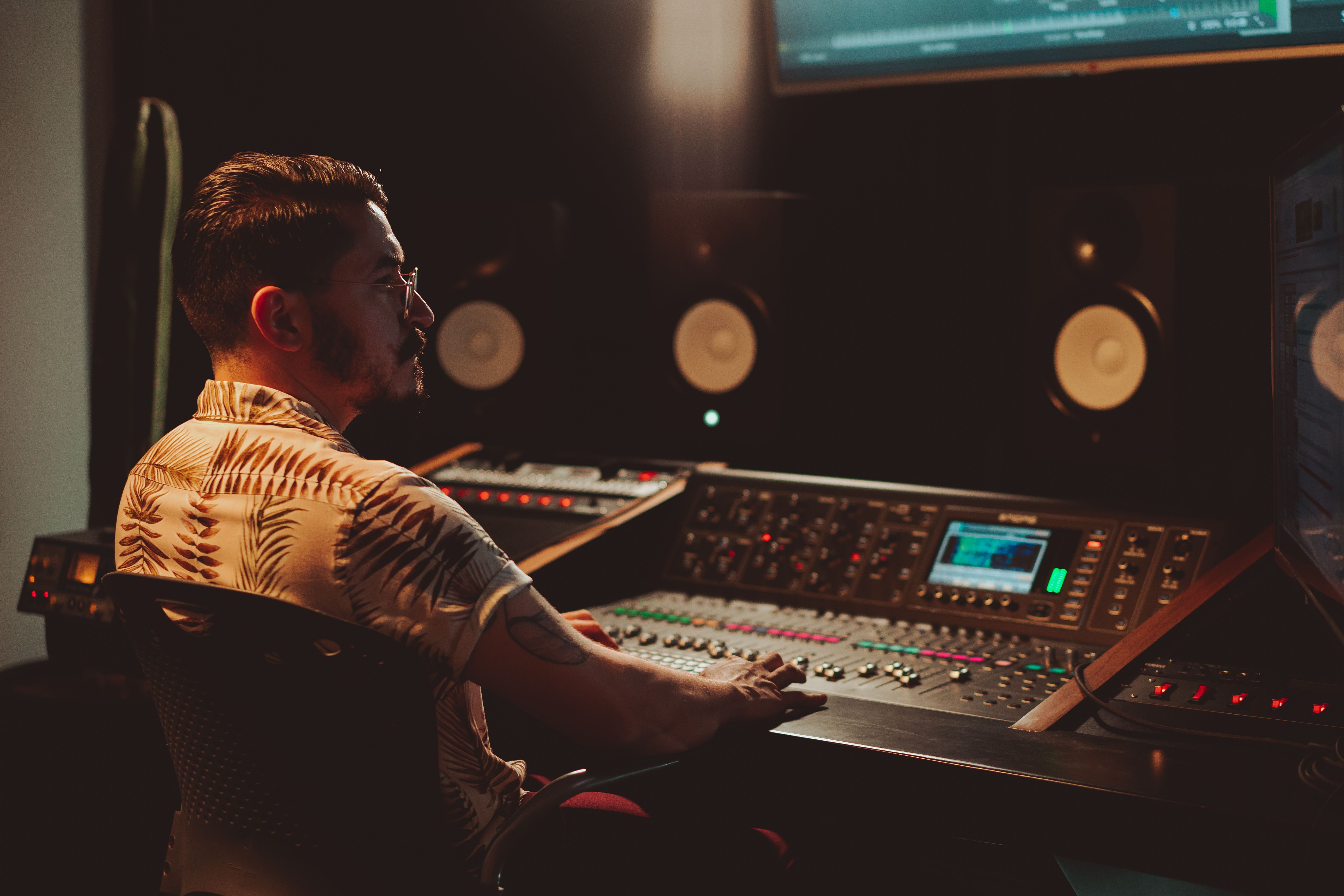Audio engineer focused on mixing at a professional sound console in a dimly lit recording studio.
