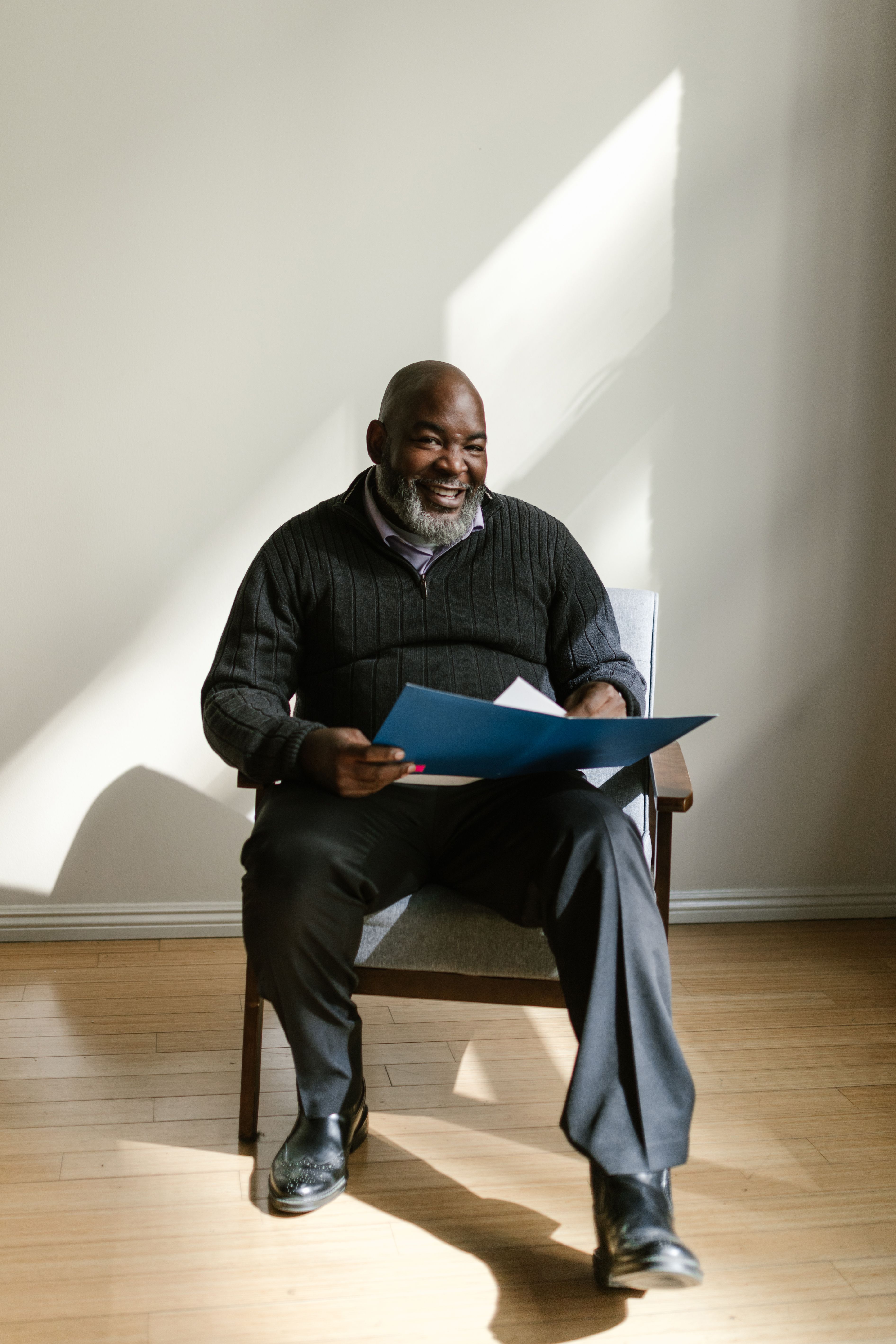 A cheerful man with a folder sits in a sunlit room, exuding positivity and warmth.