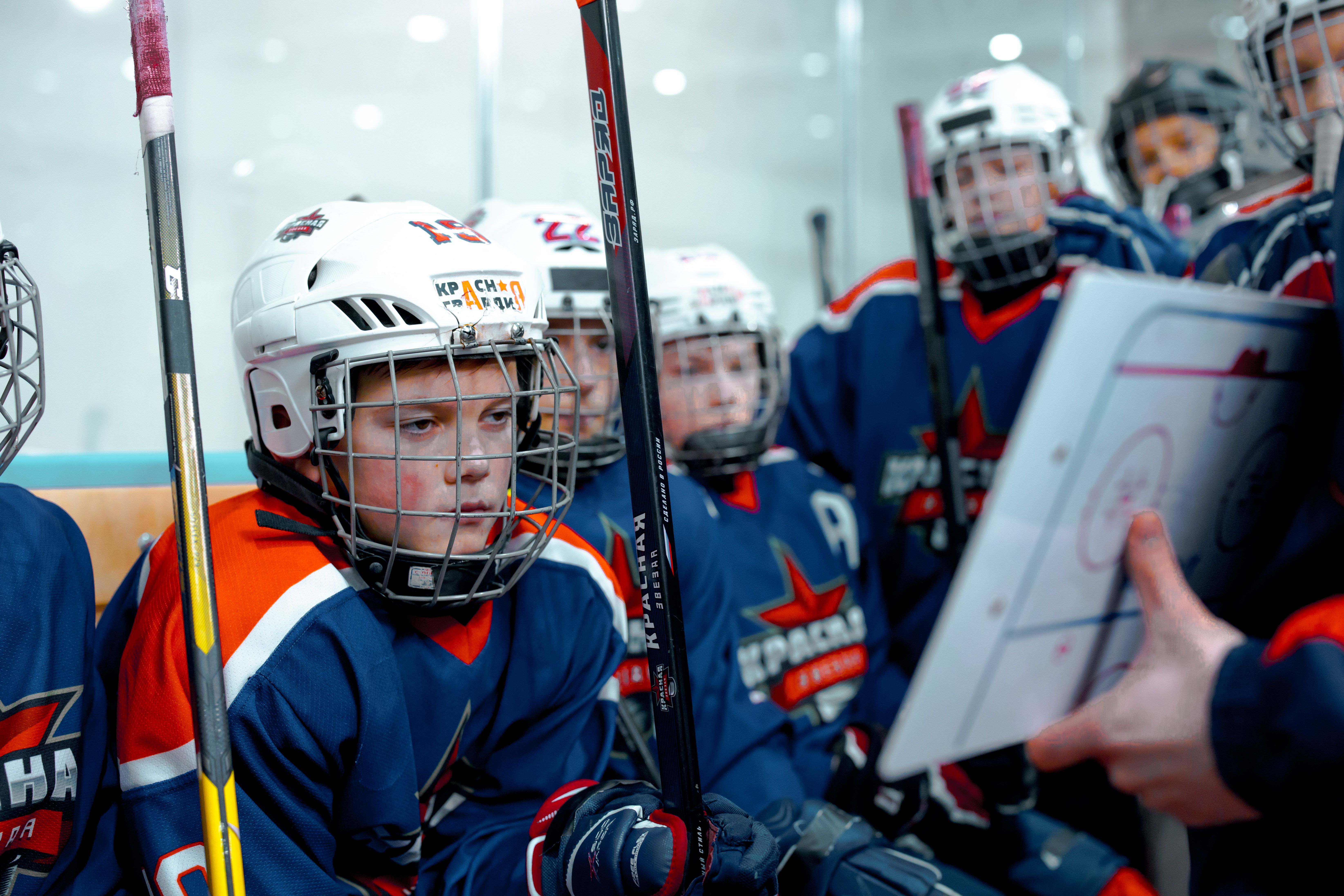 Young hockey players listen to coach's strategy during an ice hockey game in an indoor arena.